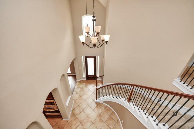 foyer entrance with light tile patterned floors, arched walkways, stairs, a high ceiling, and a notable chandelier