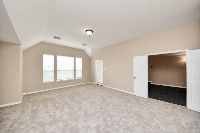 carpeted empty room with baseboards, visible vents, and vaulted ceiling