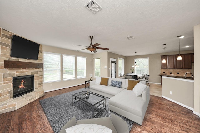 living room featuring baseboards, visible vents, wood finished floors, a textured ceiling, and a fireplace