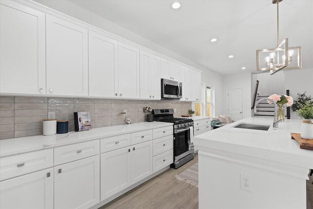 kitchen with tasteful backsplash, light wood-style flooring, appliances with stainless steel finishes, white cabinets, and a sink