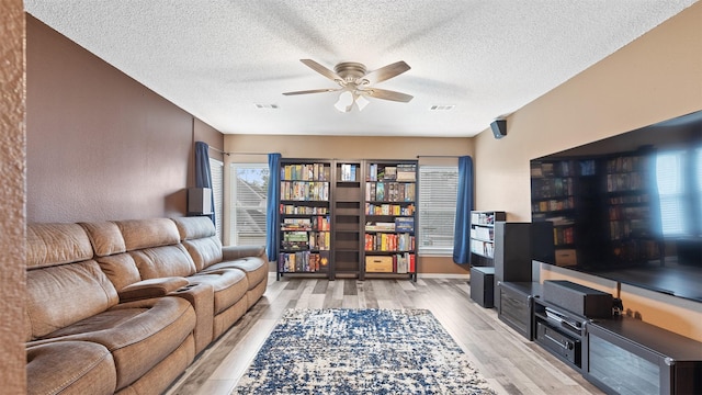 living area with ceiling fan, light wood finished floors, a textured ceiling, and visible vents