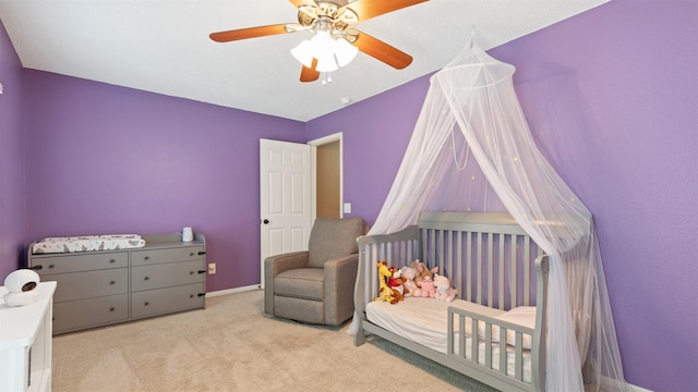 carpeted bedroom with a crib, ceiling fan, and baseboards