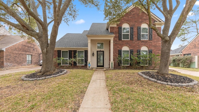 traditional home featuring a shingled roof, a front yard, and brick siding