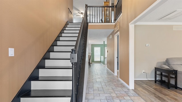 stairway featuring visible vents, baseboards, a towering ceiling, ornamental molding, and stone finish flooring