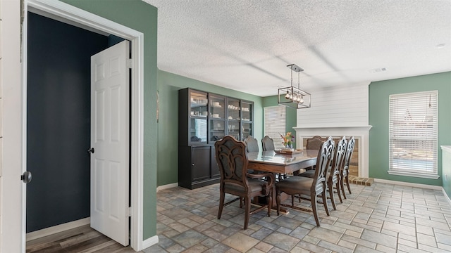 dining area with stone finish flooring, a notable chandelier, a textured ceiling, and baseboards