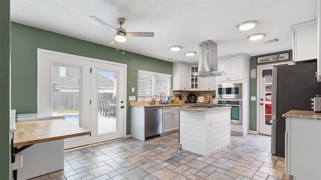 kitchen with island range hood, stainless steel appliances, a sink, visible vents, and stone finish flooring