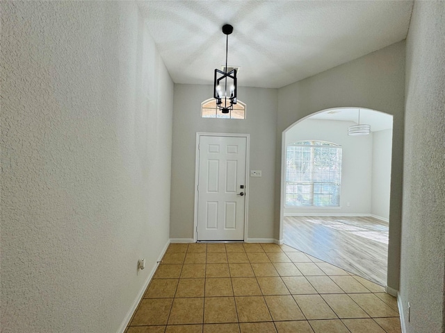 entryway featuring light tile patterned floors, a textured wall, a chandelier, arched walkways, and baseboards