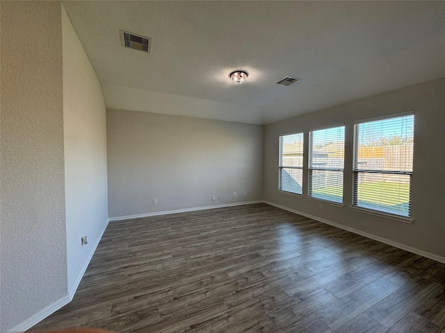 unfurnished room featuring dark wood-style flooring, visible vents, and baseboards