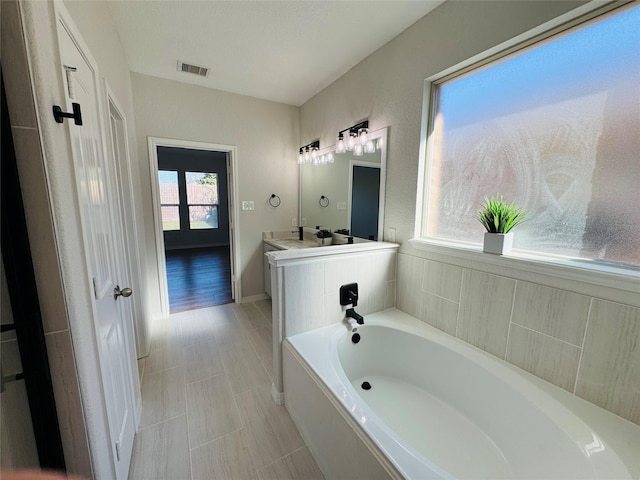 full bathroom with baseboards, visible vents, a bath, and vanity