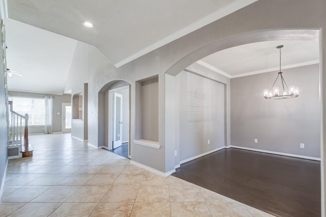 empty room featuring arched walkways, tile patterned flooring, ceiling fan with notable chandelier, baseboards, and crown molding