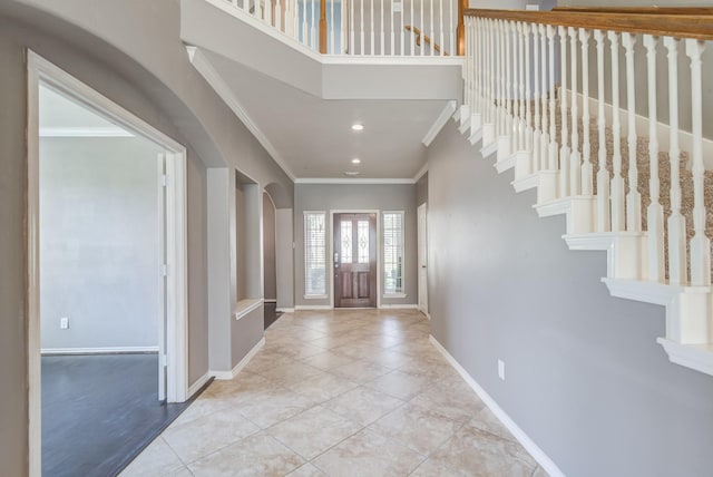 foyer with ornamental molding, arched walkways, baseboards, and tile patterned floors