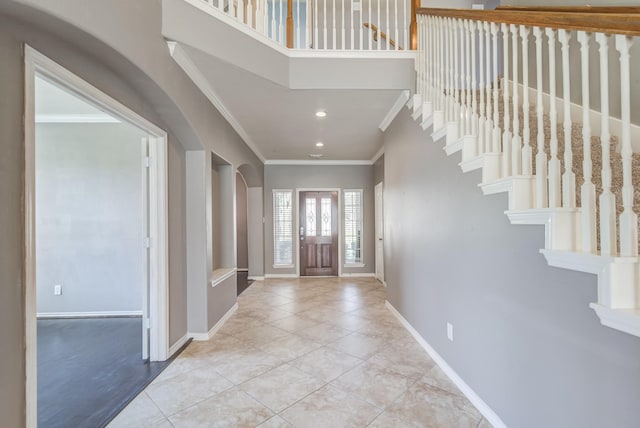 entryway with arched walkways, ornamental molding, tile patterned flooring, and baseboards