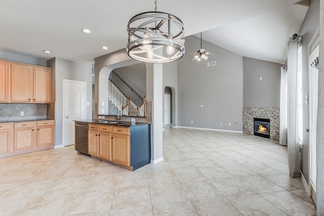 kitchen with arched walkways, a tiled fireplace, stainless steel dishwasher, open floor plan, and a sink