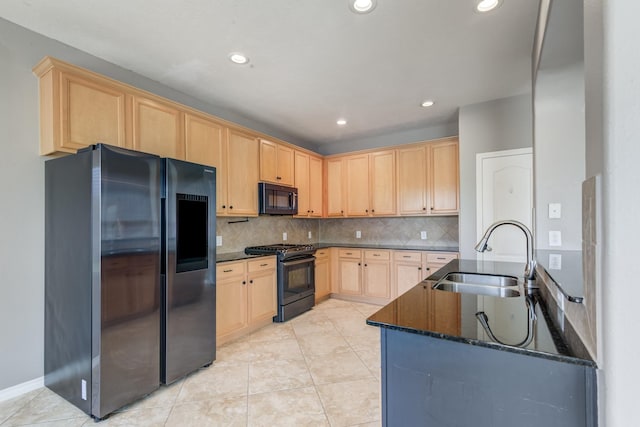 kitchen featuring tasteful backsplash, dark stone counters, light brown cabinetry, black appliances, and a sink