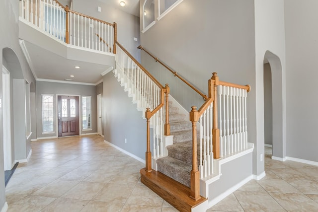 entrance foyer featuring arched walkways, a high ceiling, baseboards, tile patterned floors, and crown molding