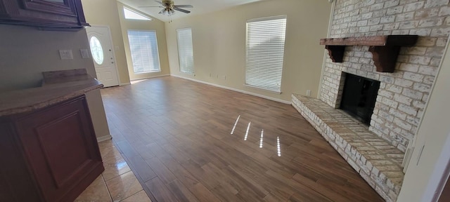 unfurnished living room featuring a fireplace, baseboards, a ceiling fan, and wood finished floors