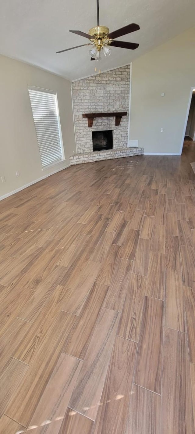 unfurnished living room with ceiling fan, a fireplace, baseboards, and wood finished floors