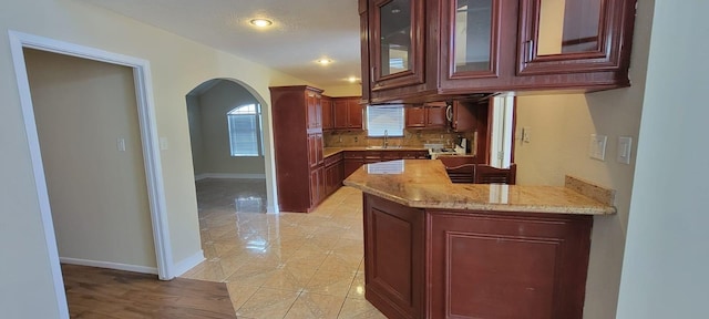 kitchen featuring arched walkways, light tile patterned flooring, a peninsula, a sink, and tasteful backsplash