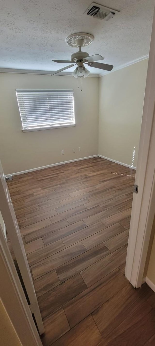 spare room with a textured ceiling, wood finished floors, visible vents, baseboards, and a ceiling fan