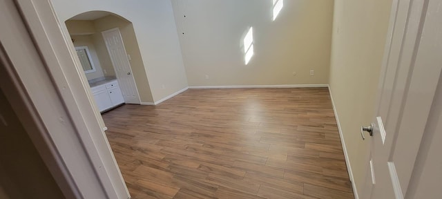 spare room with baseboards, arched walkways, and wood finished floors