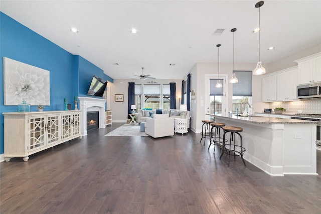 kitchen featuring dark wood-style floors, visible vents, appliances with stainless steel finishes, white cabinets, and a warm lit fireplace