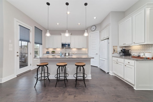 kitchen with a breakfast bar, stainless steel microwave, freestanding refrigerator, and white cabinets