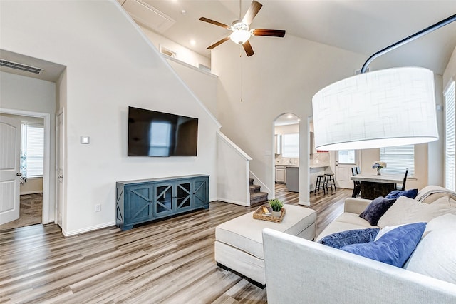 living room featuring stairway, wood finished floors, baseboards, high vaulted ceiling, and ceiling fan