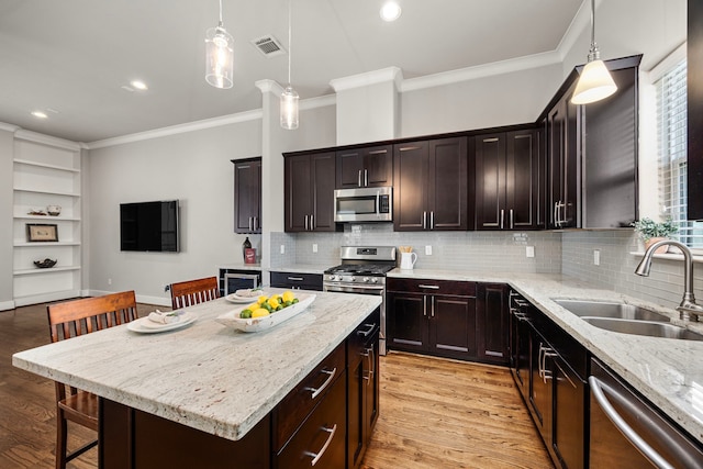 kitchen with visible vents, ornamental molding, stainless steel appliances, light wood-type flooring, and a sink