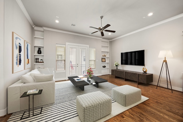 living room with built in shelves, wood finished floors, visible vents, baseboards, and ornamental molding