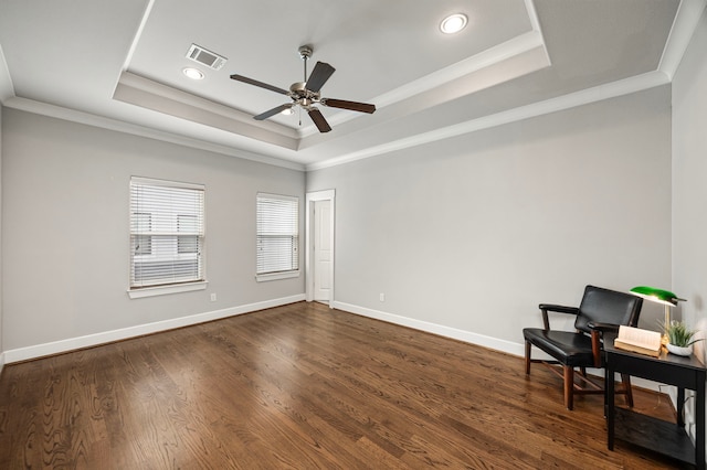 living area with dark wood-type flooring, visible vents, baseboards, a tray ceiling, and crown molding