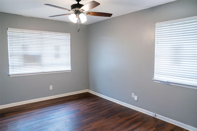 spare room featuring a healthy amount of sunlight, dark wood-style floors, ceiling fan, and baseboards