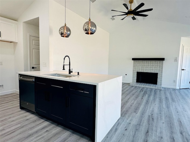 kitchen with a fireplace with raised hearth, dark cabinets, a sink, light countertops, and dishwasher