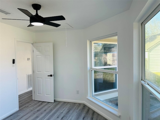 unfurnished room with a wealth of natural light, wood finished floors, visible vents, and attic access