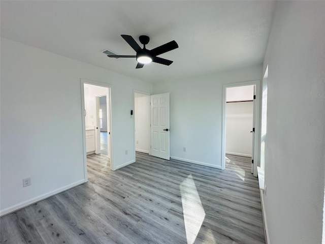 unfurnished bedroom featuring visible vents, baseboards, a ceiling fan, wood finished floors, and a walk in closet