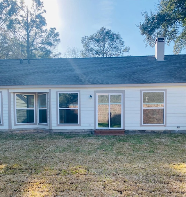 back of property featuring a yard, a shingled roof, and a chimney