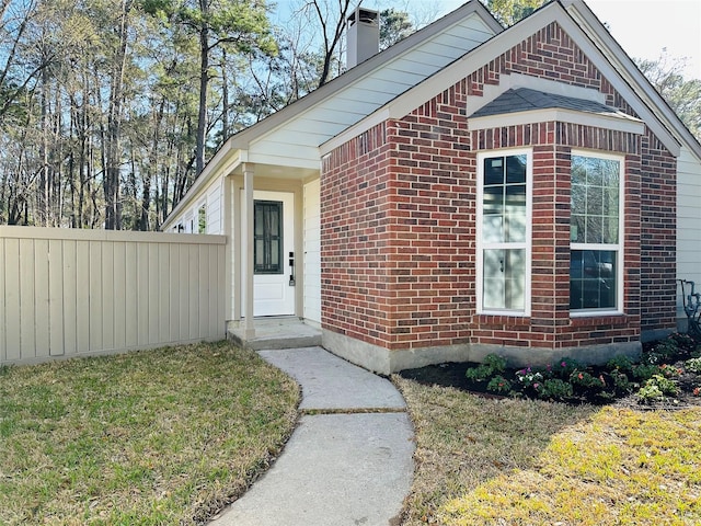 exterior space featuring brick siding, fence, a chimney, and a lawn