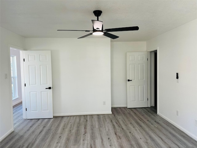 unfurnished bedroom featuring ceiling fan, a textured ceiling, baseboards, and wood finished floors