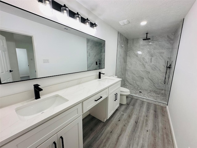 bathroom with wood finished floors, tiled shower, a sink, and toilet