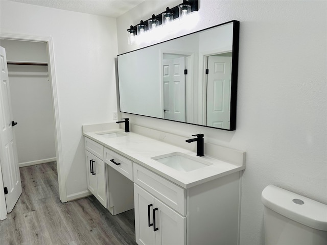 full bathroom featuring double vanity, wood finished floors, a sink, and toilet