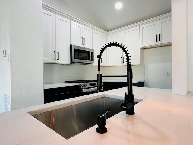 interior space featuring stainless steel microwave, backsplash, white cabinetry, and light stone countertops