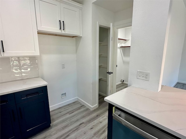 interior space with white cabinets, light stone counters, light wood-type flooring, stainless steel dishwasher, and backsplash