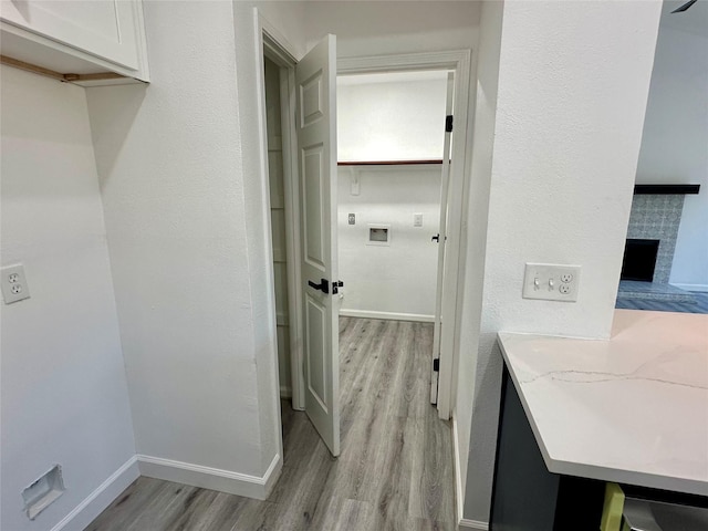 laundry area with light wood-style floors, a fireplace with raised hearth, and baseboards