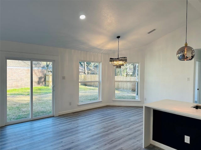 unfurnished dining area featuring an inviting chandelier, plenty of natural light, visible vents, and wood finished floors