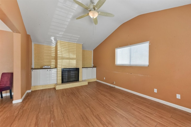 unfurnished living room with lofted ceiling, a ceiling fan, wood finished floors, baseboards, and a brick fireplace