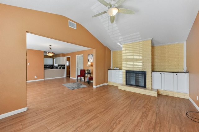 unfurnished living room featuring light wood finished floors, visible vents, a brick fireplace, and lofted ceiling