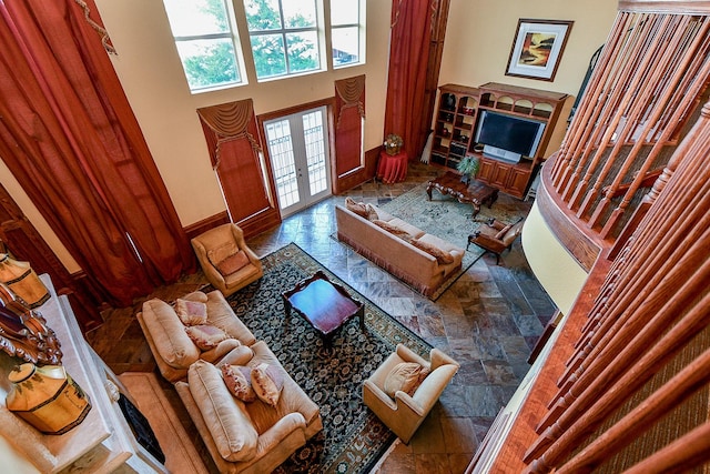 interior space with a towering ceiling, stone finish floor, baseboards, and french doors