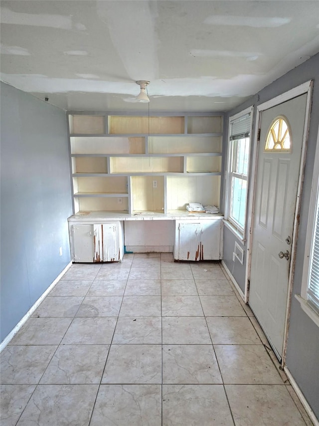 kitchen with light tile patterned flooring, baseboards, light countertops, open shelves, and built in desk