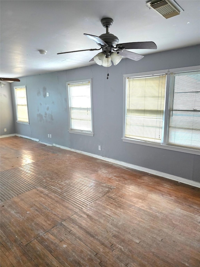 empty room featuring ceiling fan, plenty of natural light, wood-type flooring, and visible vents