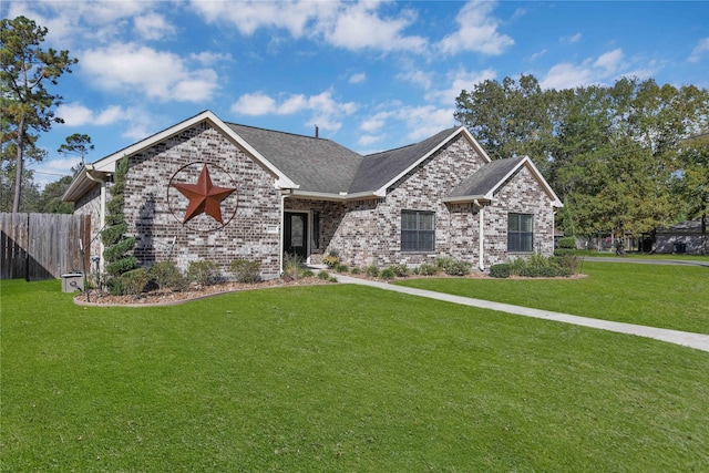 view of front of house with brick siding, a shingled roof, fence, and a front yard