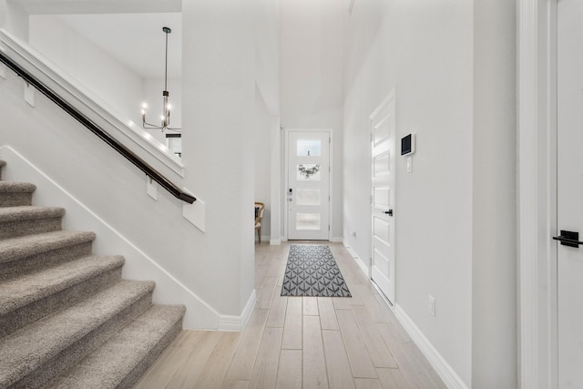 entrance foyer with stairs, light wood-type flooring, a chandelier, and baseboards